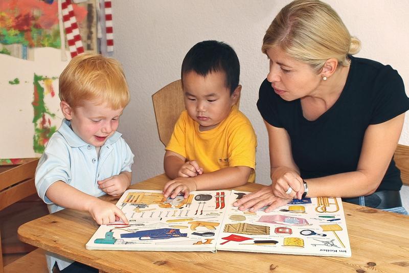 Eine Fachkraft und zwei Kindergartenkinder lesen ein Buch
