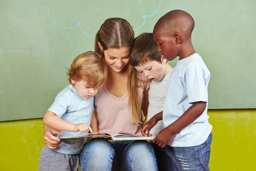 Eine Fachkraft liest ein Buch mit drei Kindergartenkindern